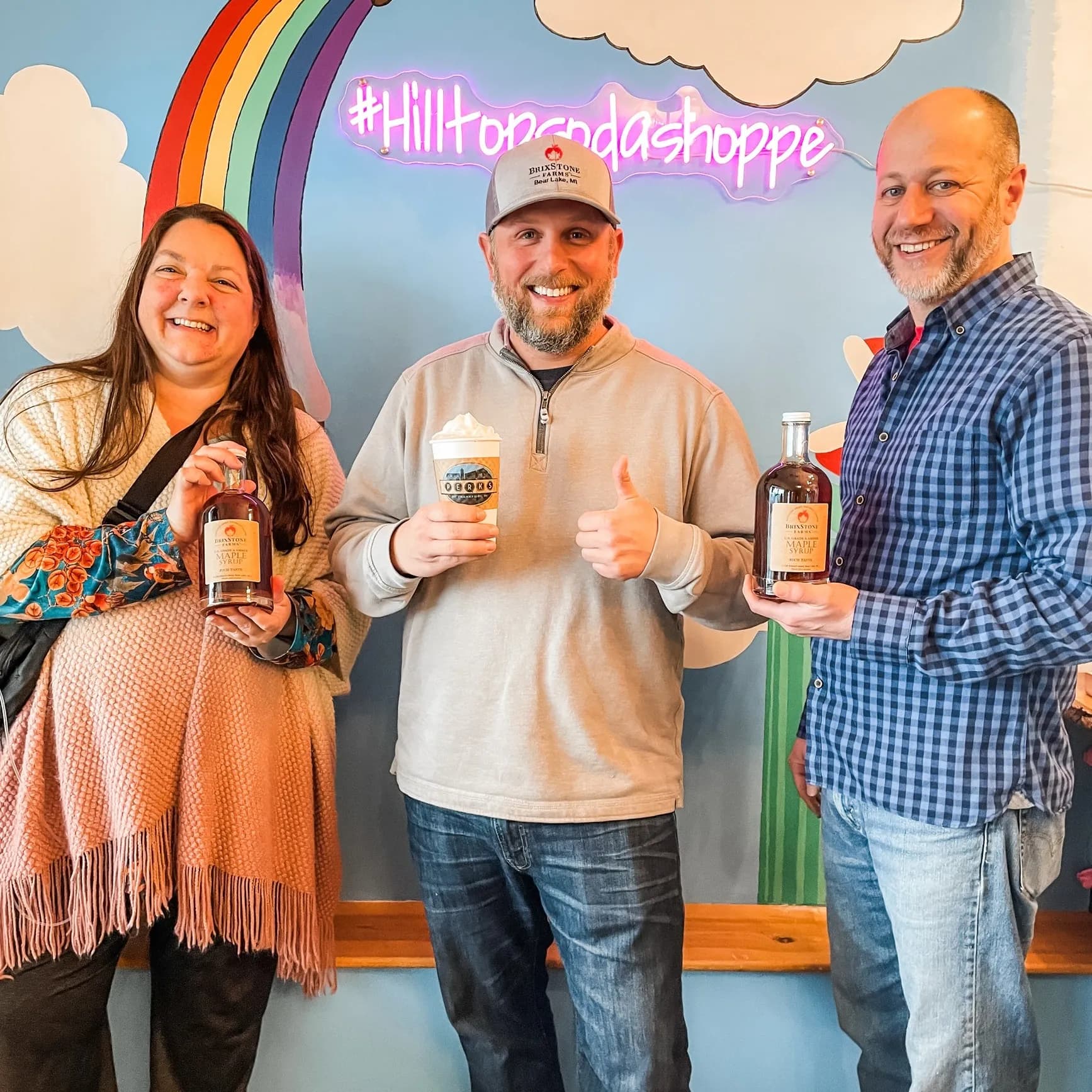 Three smiling people at Hill Top holding drinks and local maple syrup